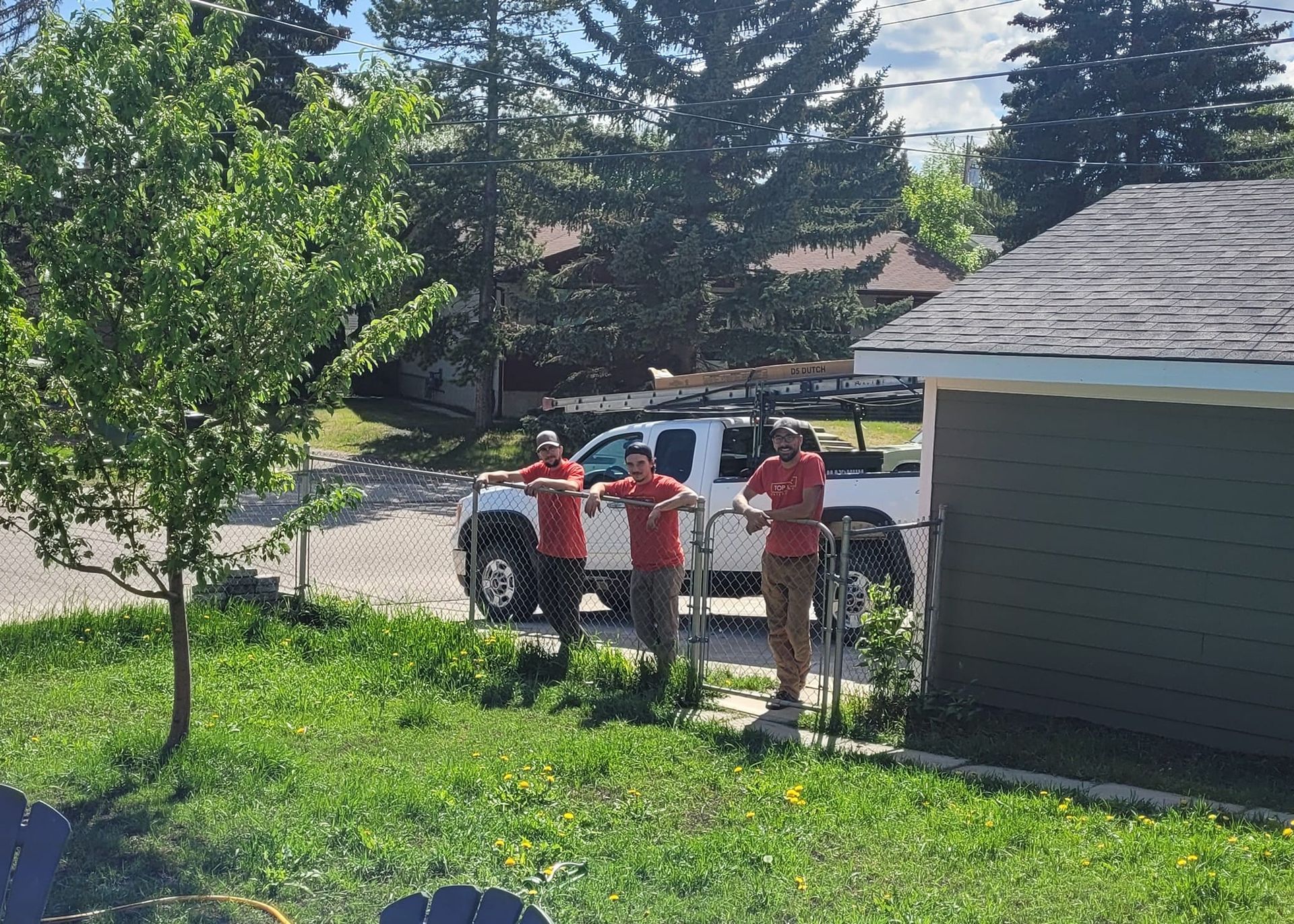 Three men are standing in front of a white truck in a yard.