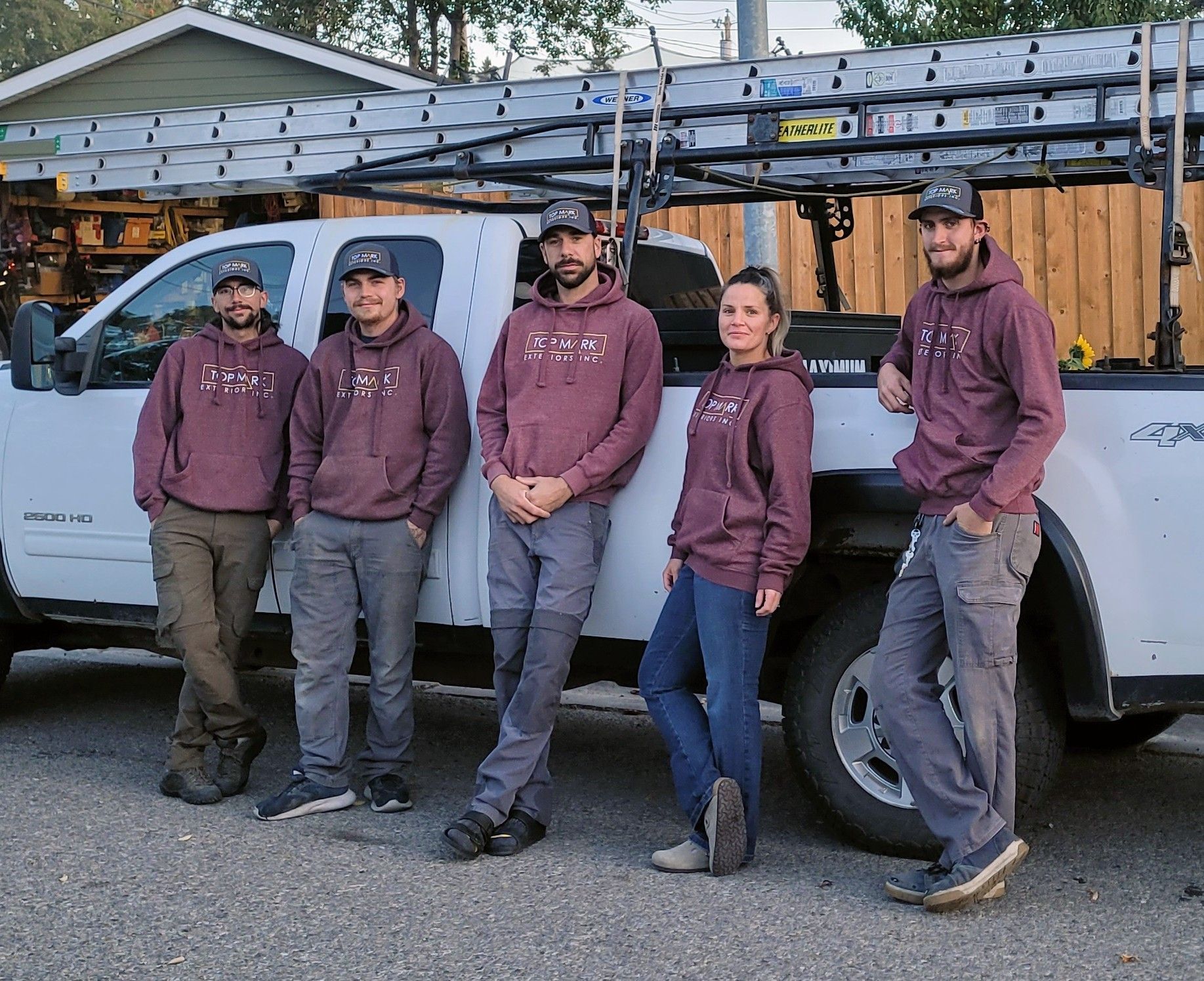 Five people in maroon hoodies pose next to a white truck with a ladder rack.