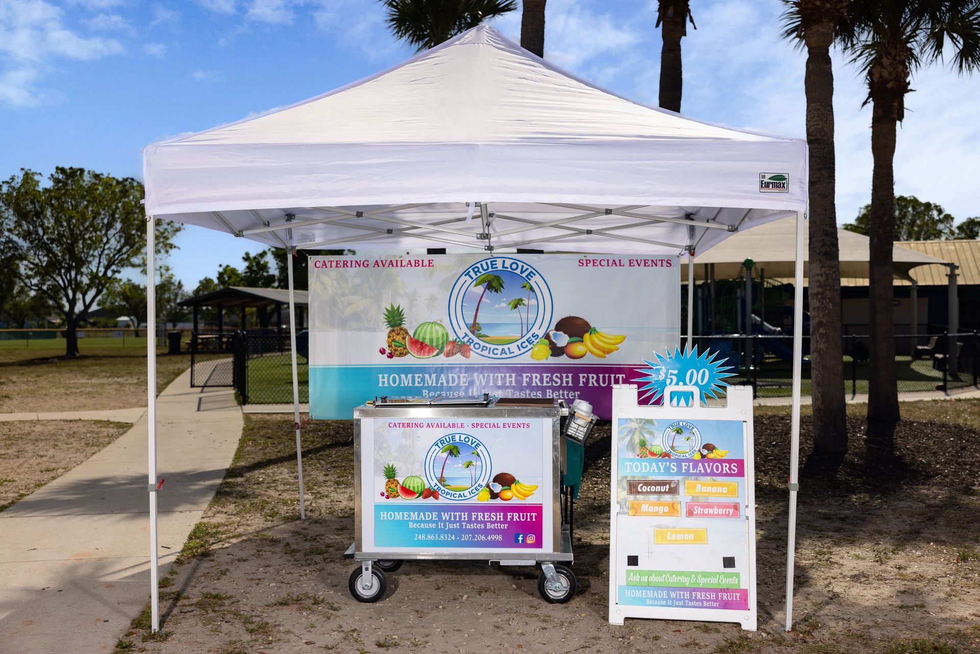 A white tent with a cart underneath it in a park.