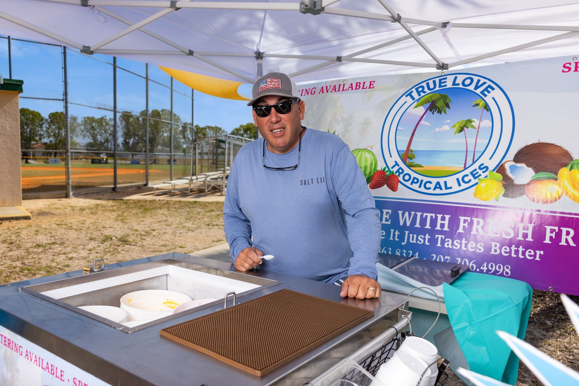 A man is standing in front of a tent selling ice cream.