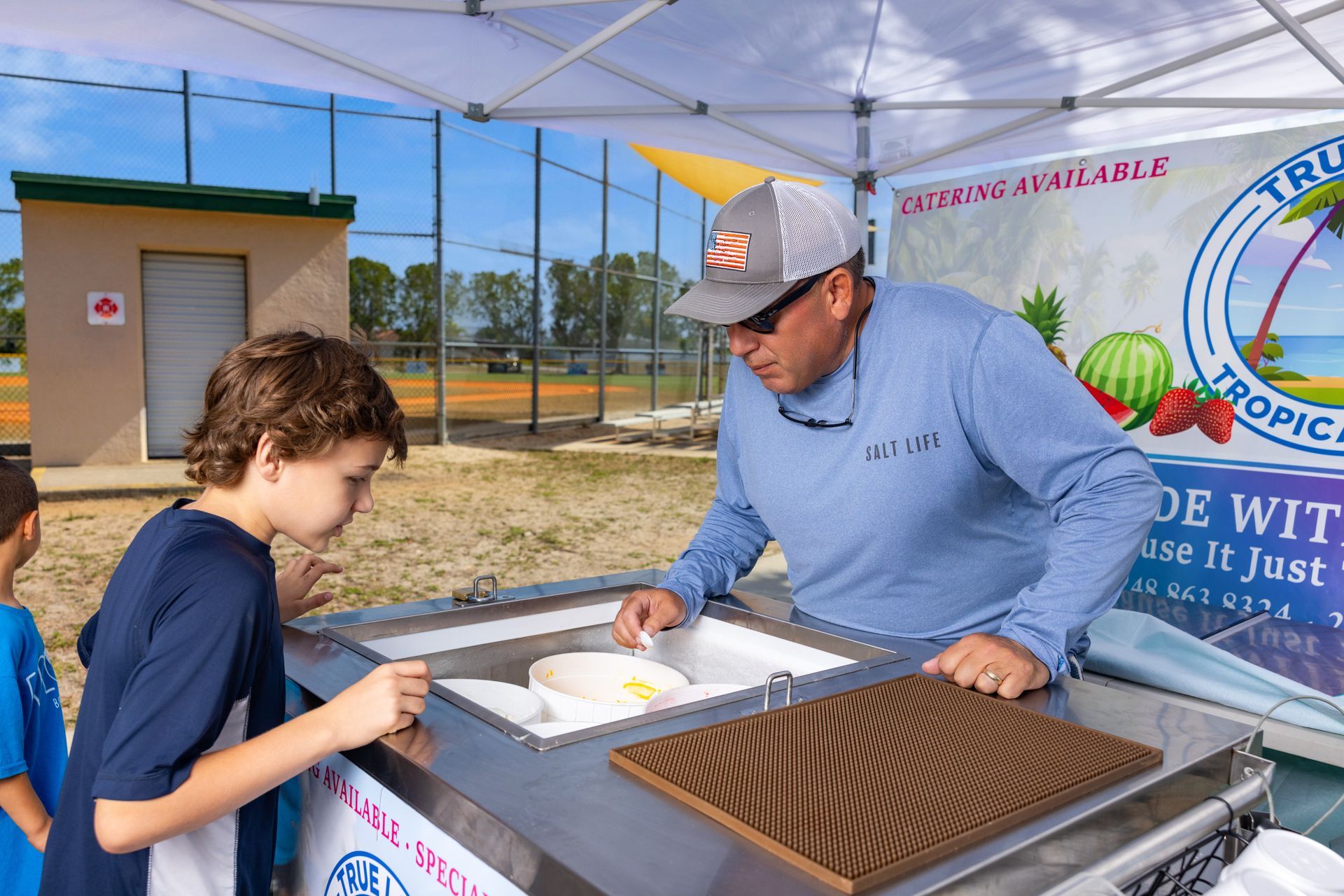 A man is serving ice cream to a boy in front of a tent.