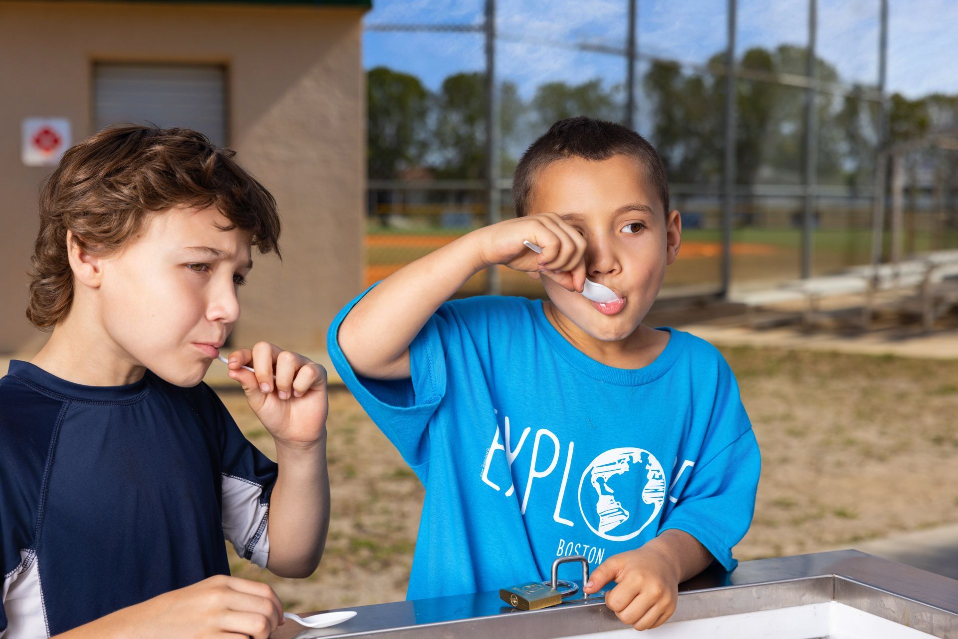 Two young boys are brushing their teeth at a water fountain.