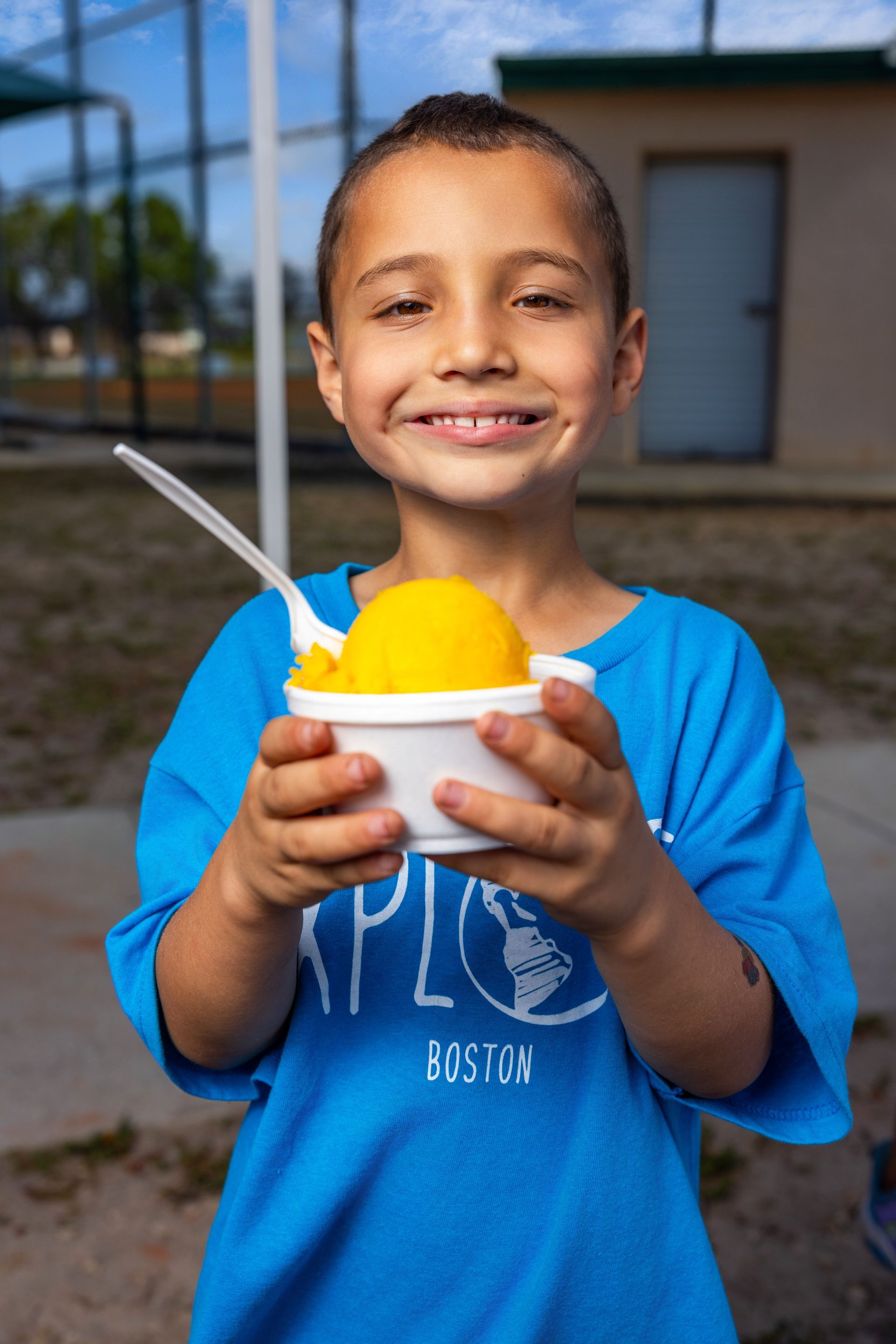 A young boy in a blue shirt is holding a bowl of ice cream.