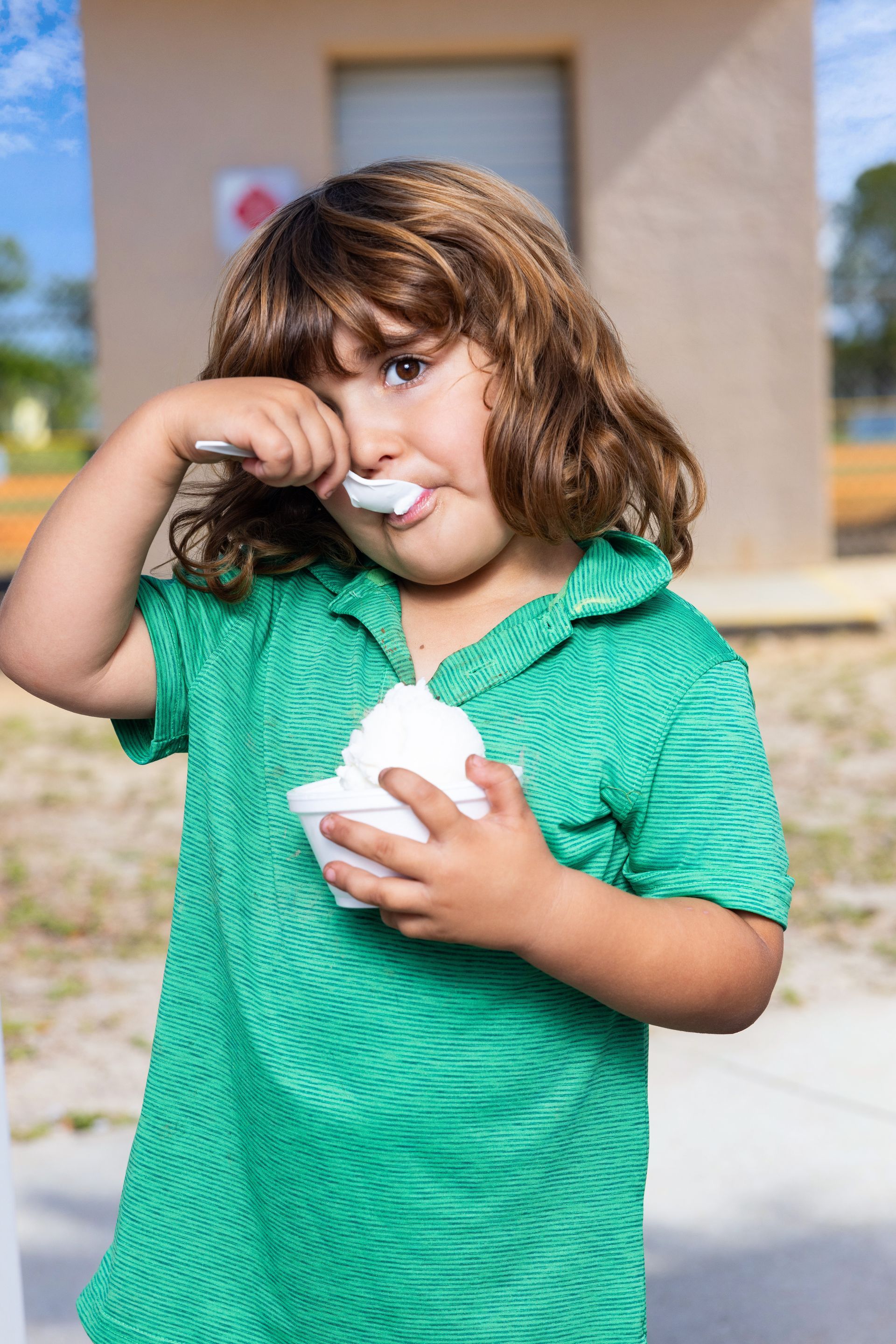 A young boy in a green shirt is eating ice cream with a spoon.