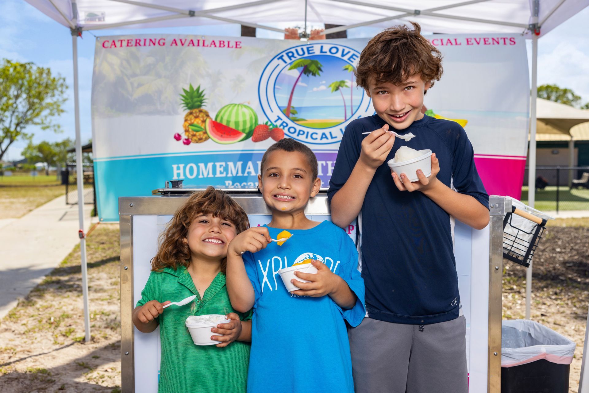Three children are standing in front of a tent eating ice cream.