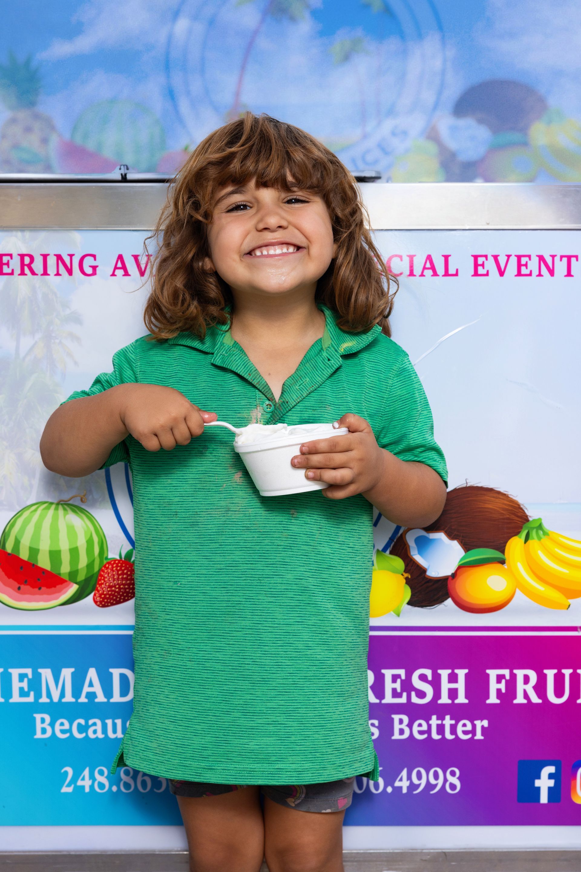 A little girl in a green dress is holding a bowl of yogurt.