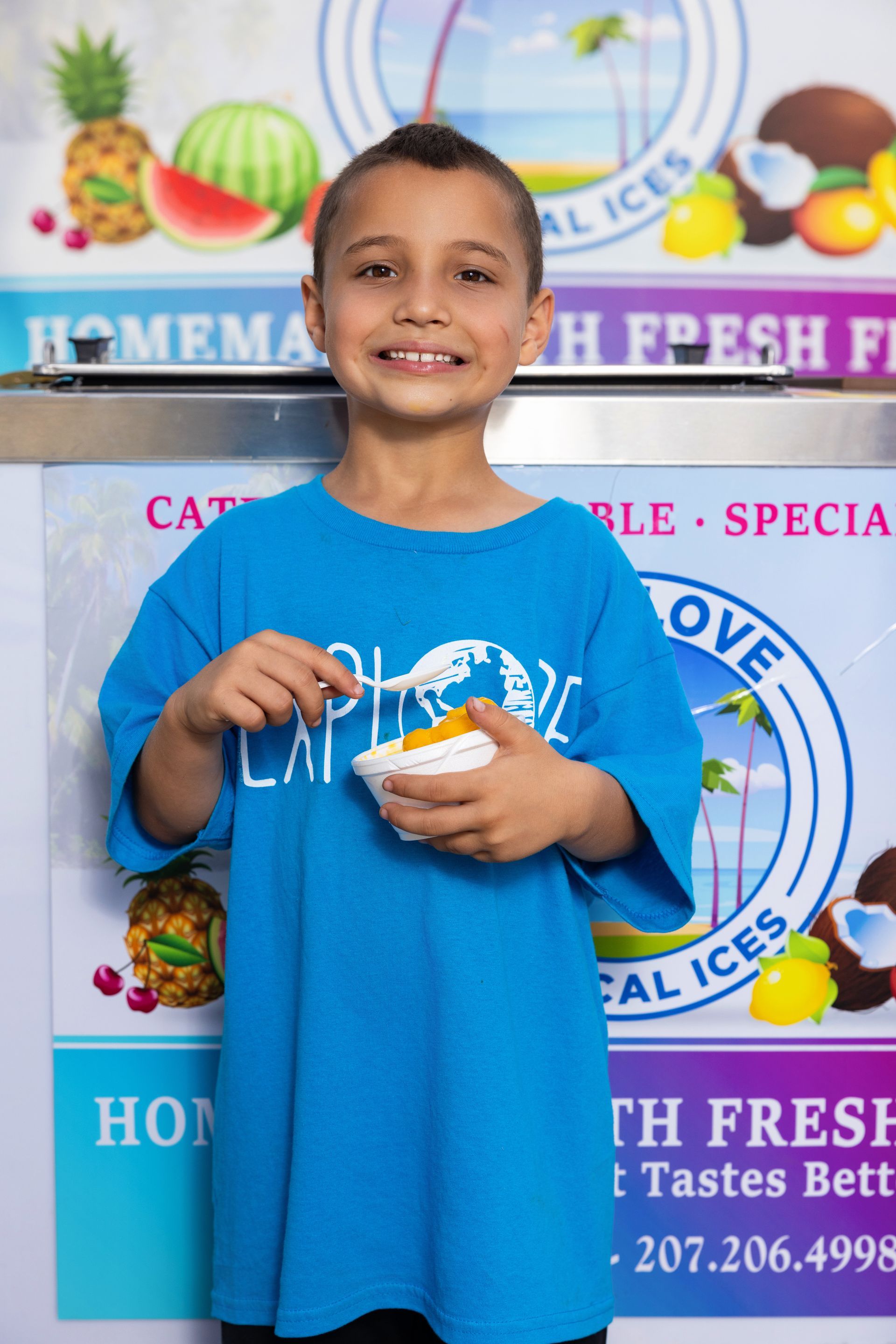 A young boy in a blue shirt is holding a cup of ice cream