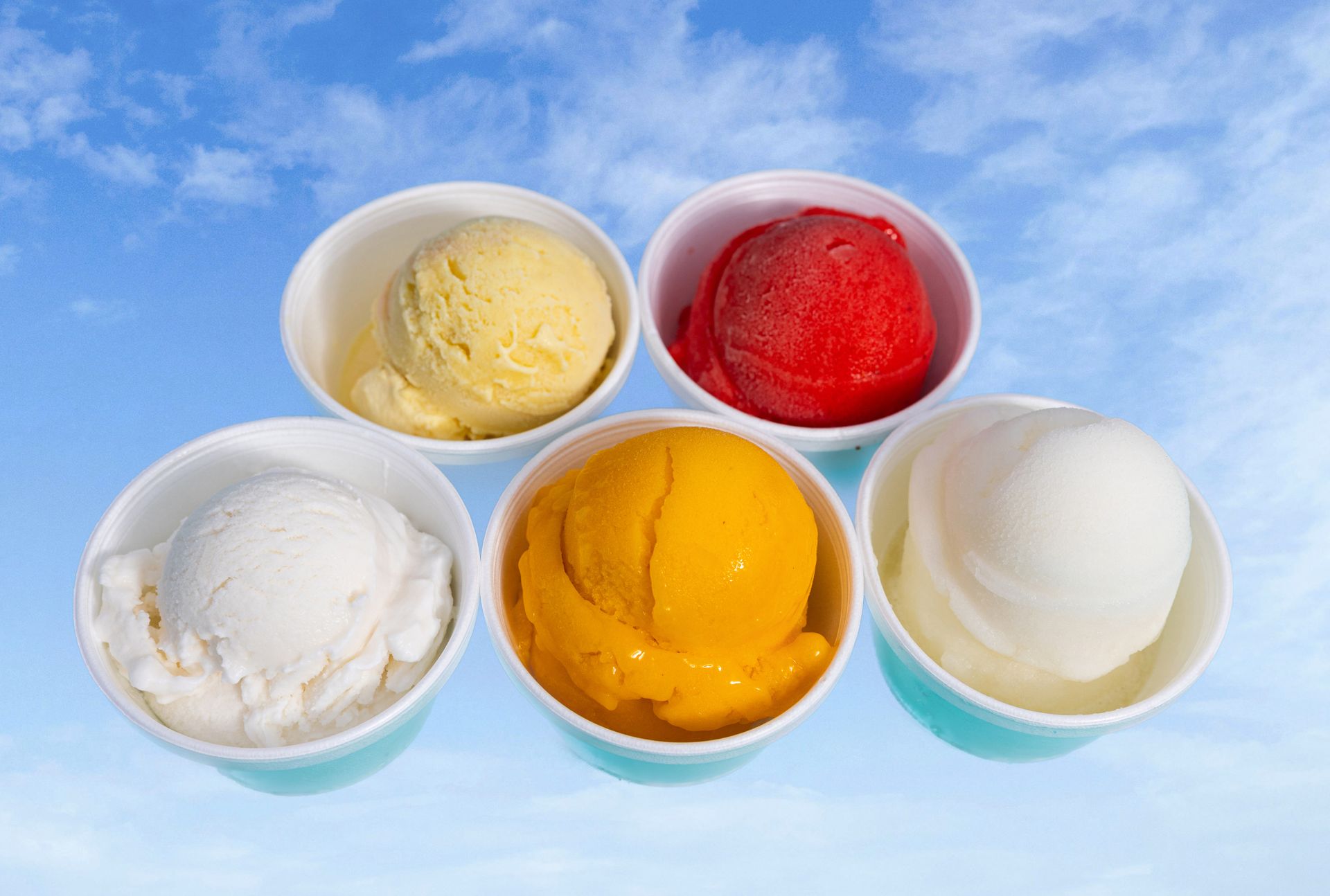 Five bowls of different flavors of ice cream against a blue sky