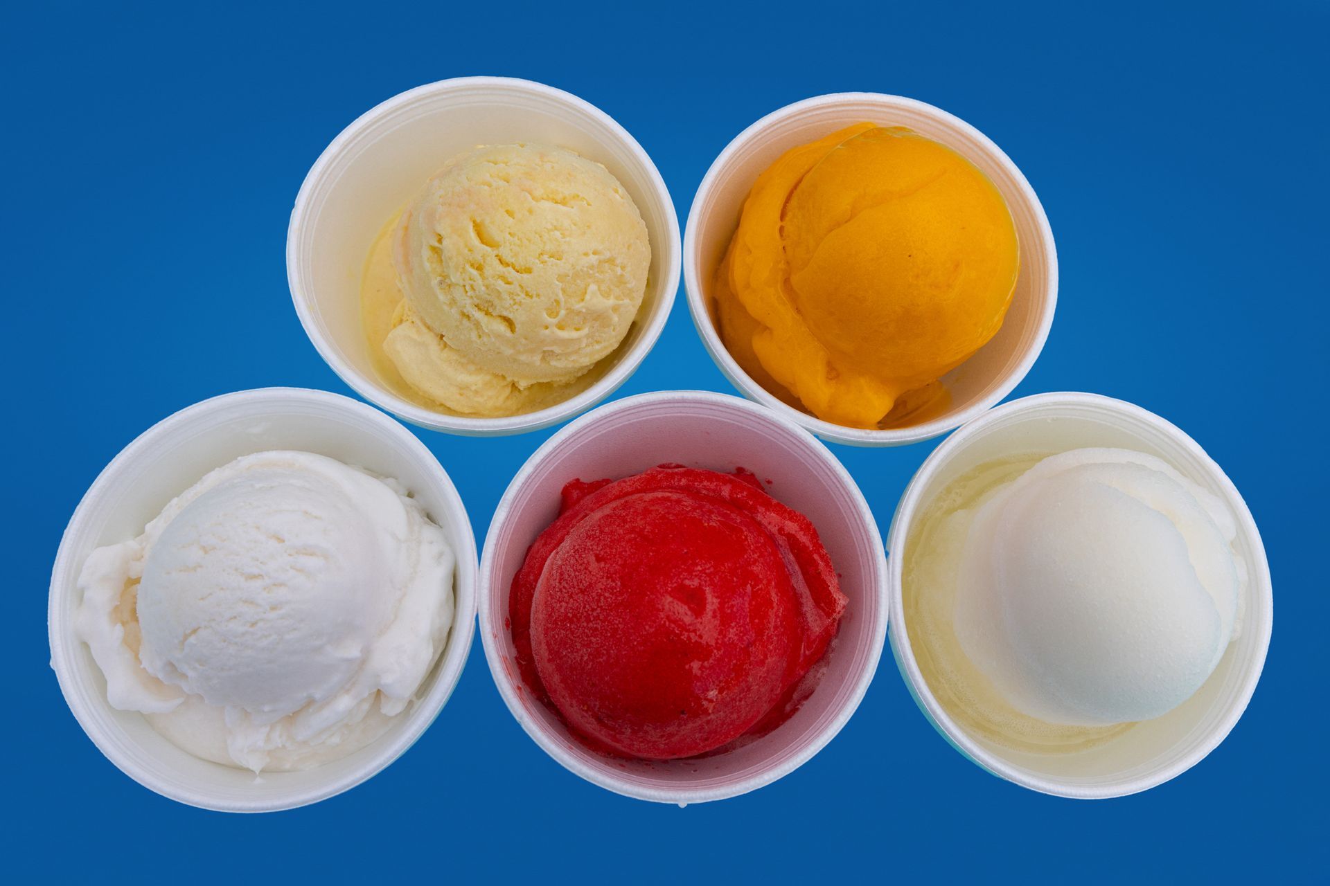 Five cups of different flavors of ice cream on a blue background