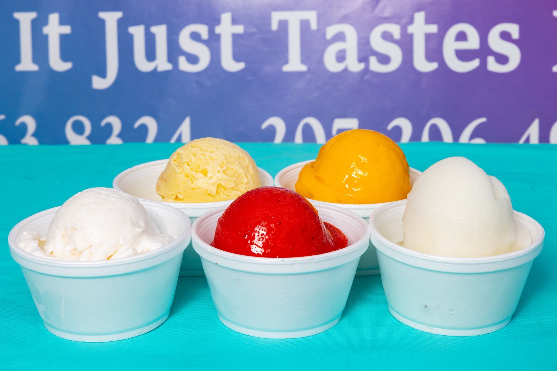 Four bowls of different flavors of ice cream are lined up in front of a sign that says it just tastes