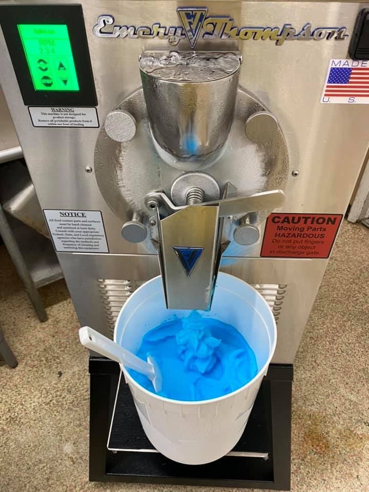 A bucket of blue ice cream is being poured into a machine.