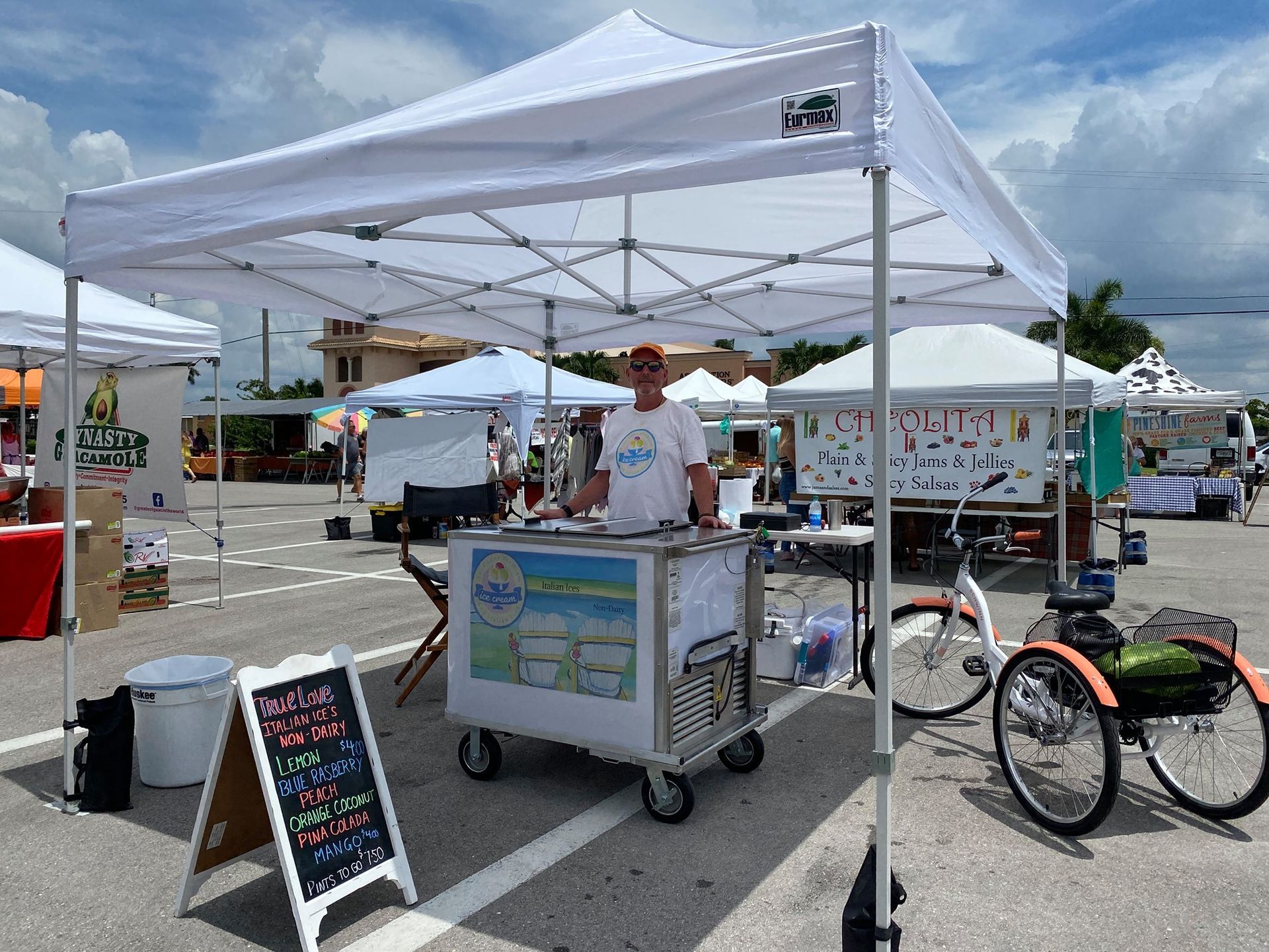 A man is standing behind an ice cream cart under a white tent.