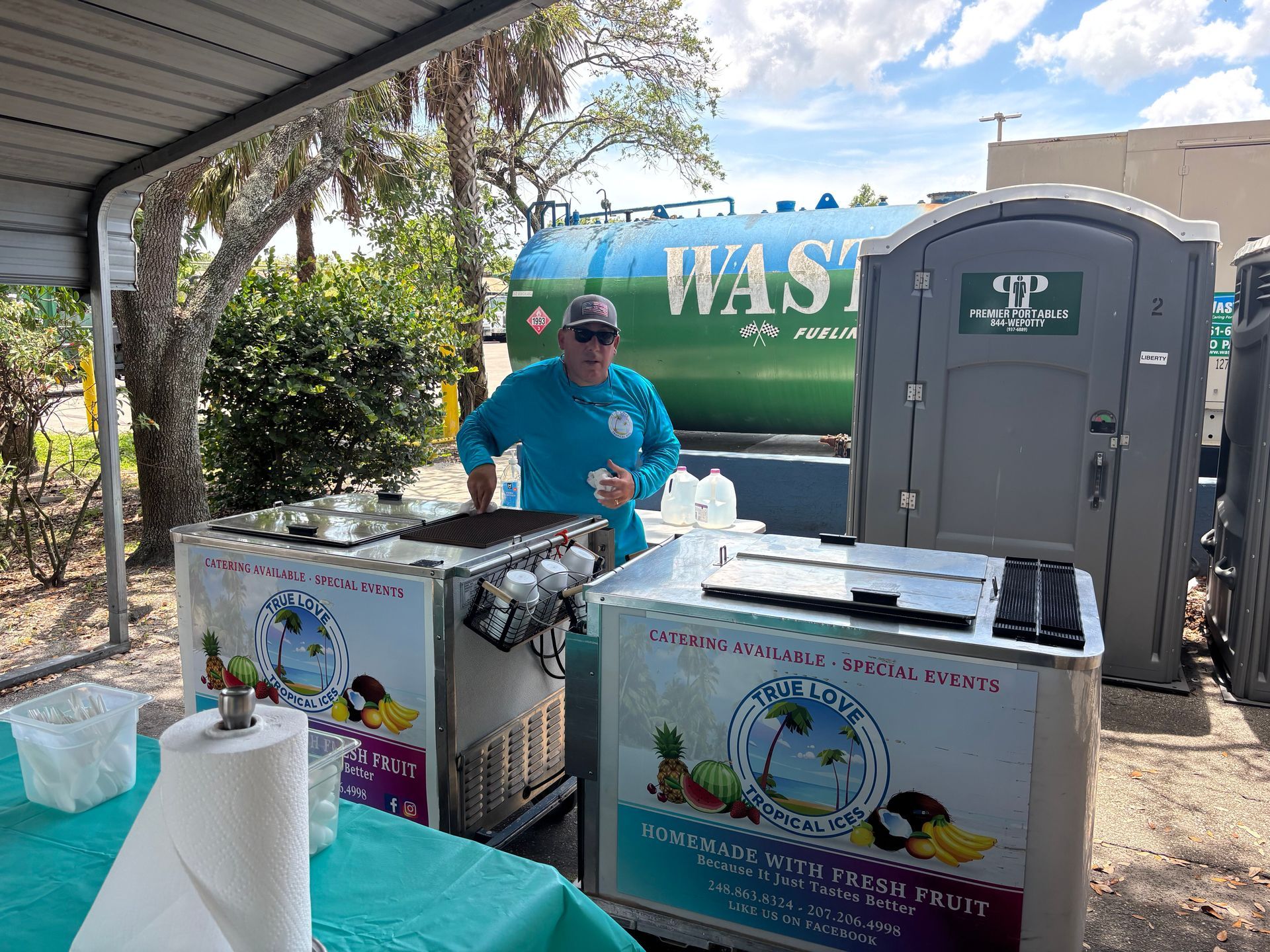 Man at shaved ice stand near portable toilet, with a 