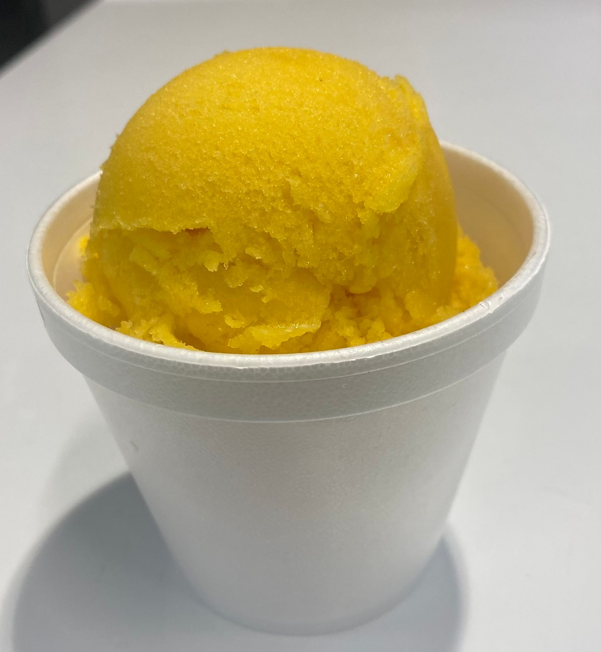 A white styrofoam cup filled with yellow ice cream