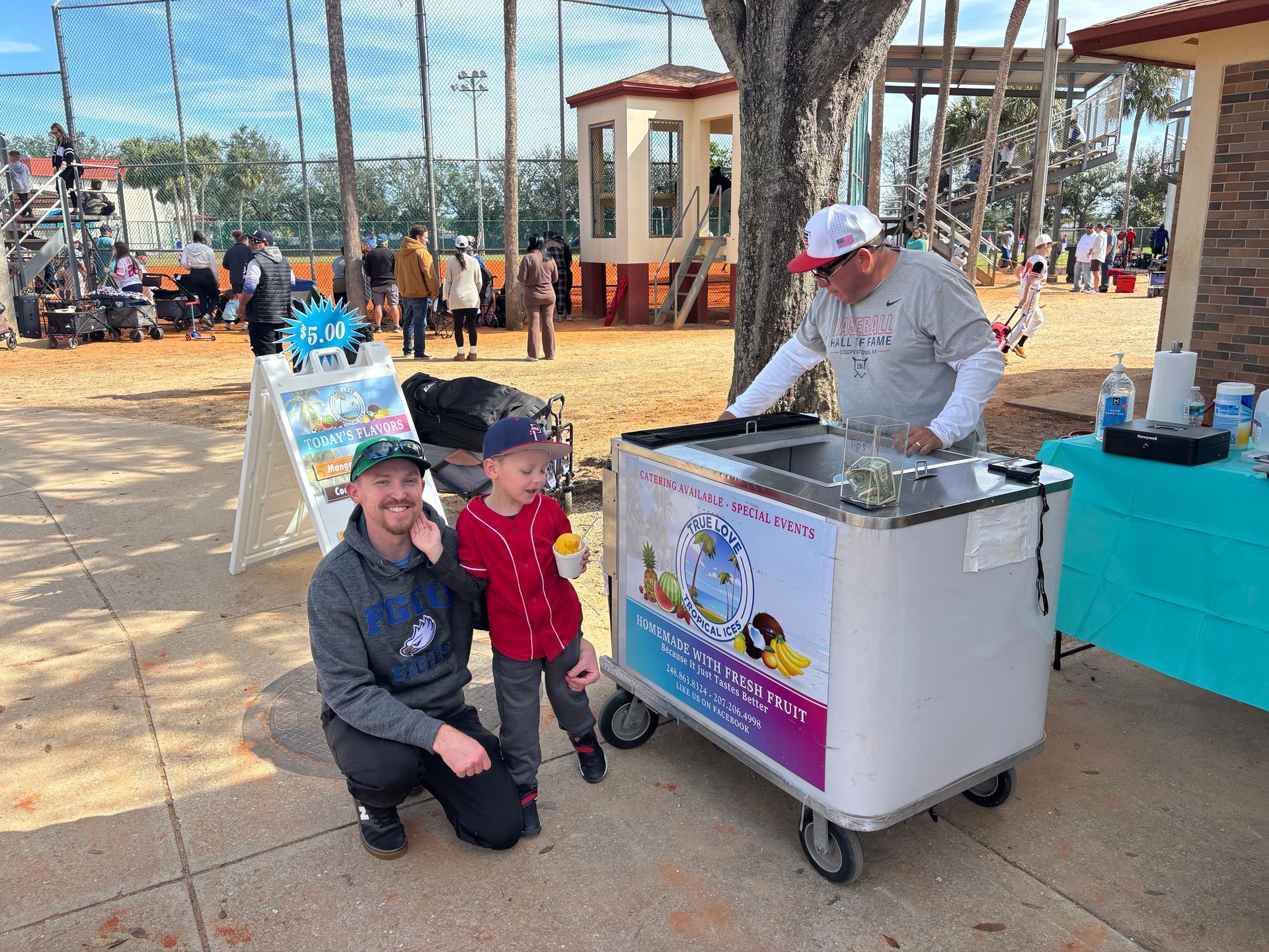 A man and a child are standing next to an ice cream cart.