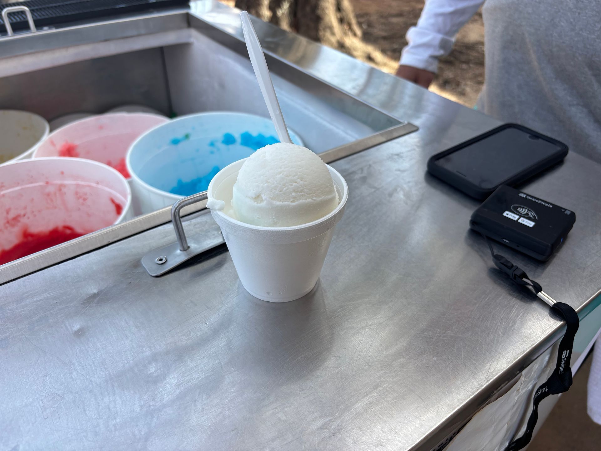 A cup of ice cream sits on a counter next to a cell phone