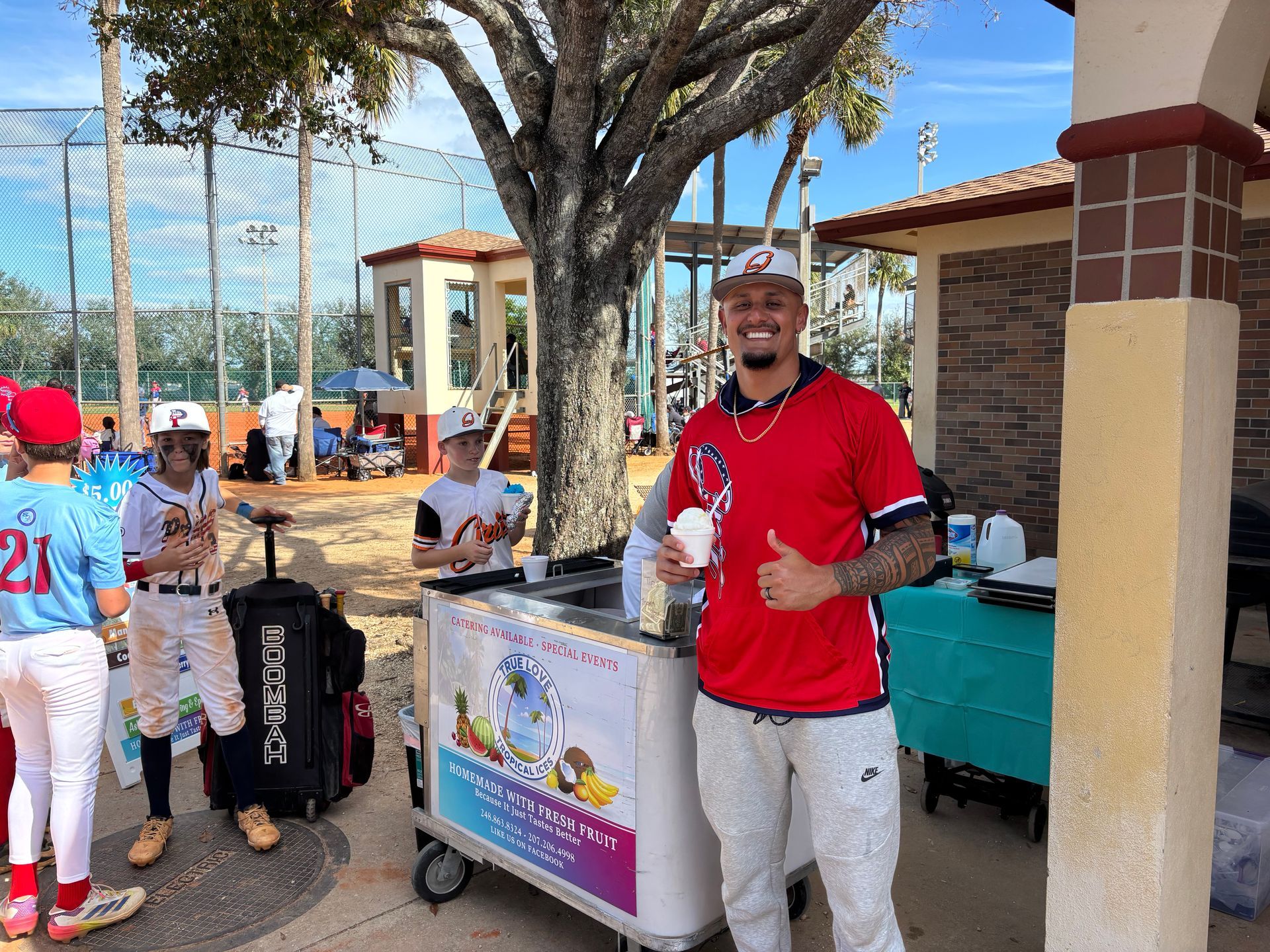 A man is standing in front of an ice cream cart giving a thumbs up.