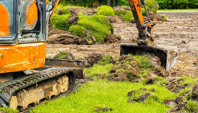 Orange excavator digging in a muddy, grassy field.