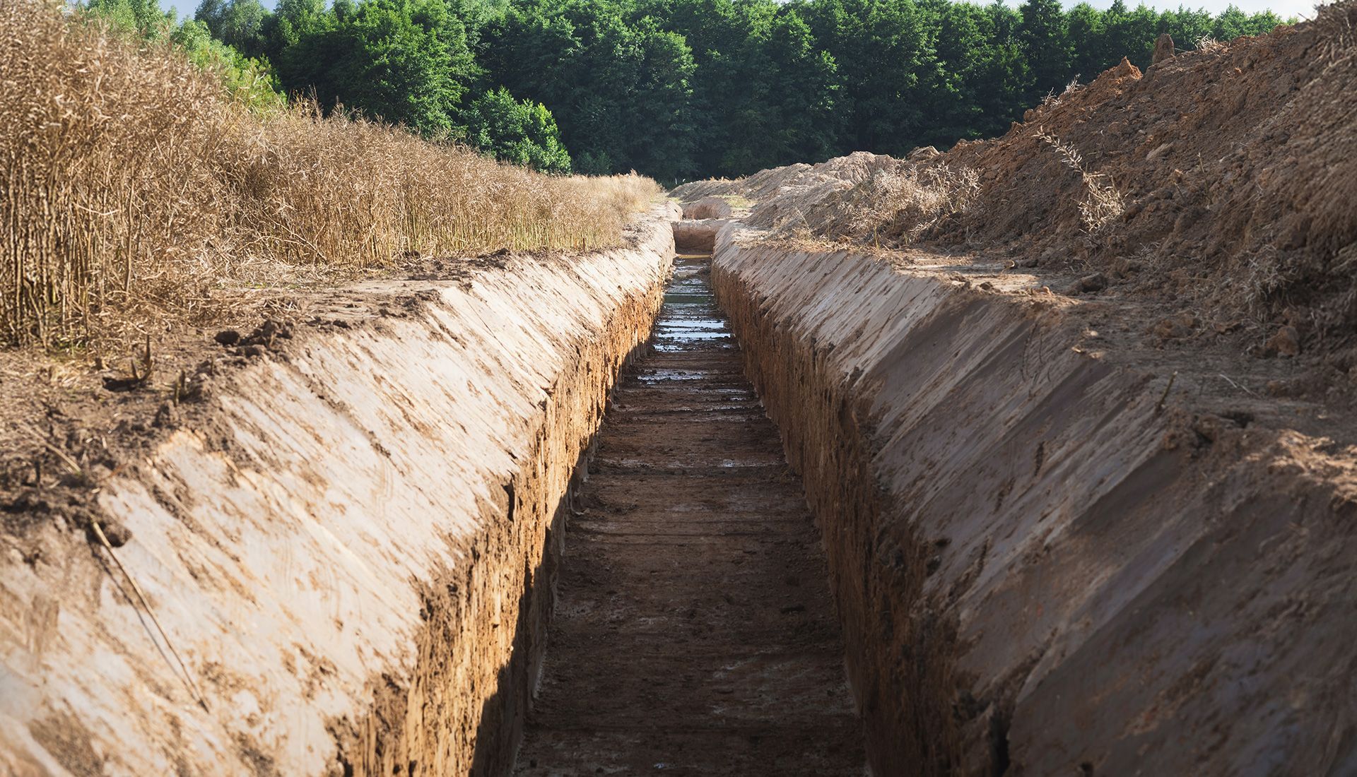 Long, narrow trench dug into dry earth, with water at bottom.