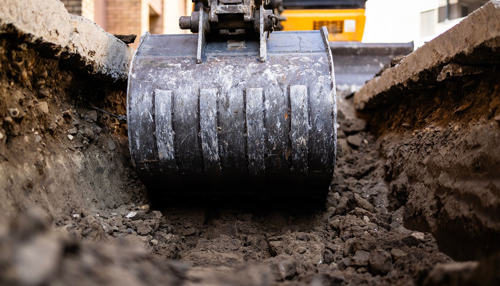 Excavator bucket digging a trench in the dirt, close-up view.
