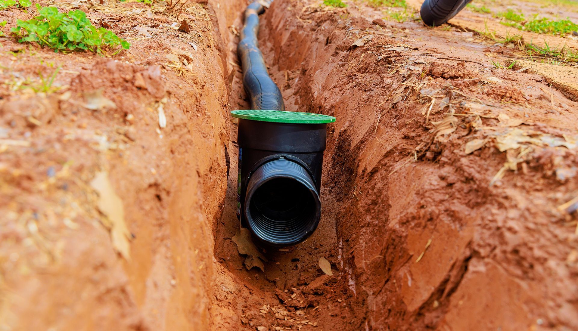 Black drainage pipe installed in an earthen trench; green cap visible.