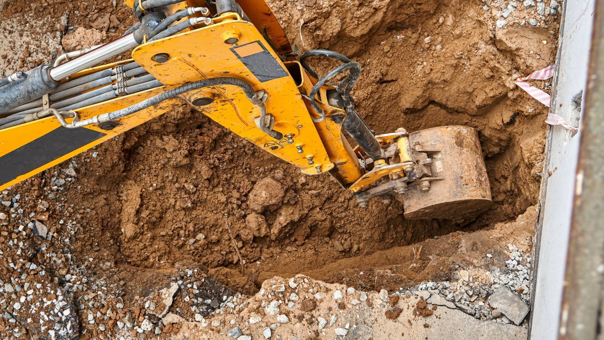 Yellow excavator digging in brown dirt next to a concrete structure.