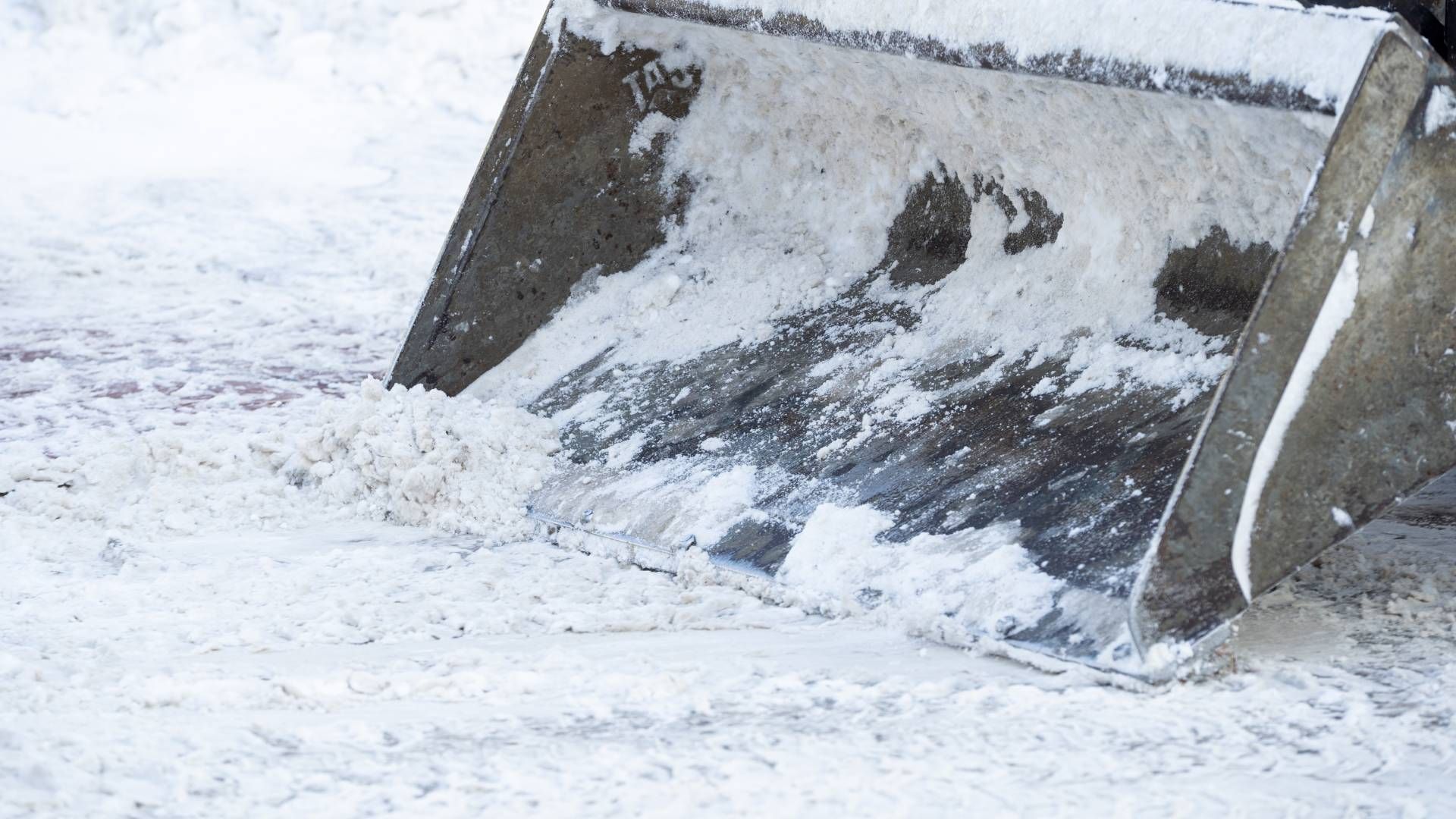 A snow-covered front-end loader scoop being used to clear snow from a surface.