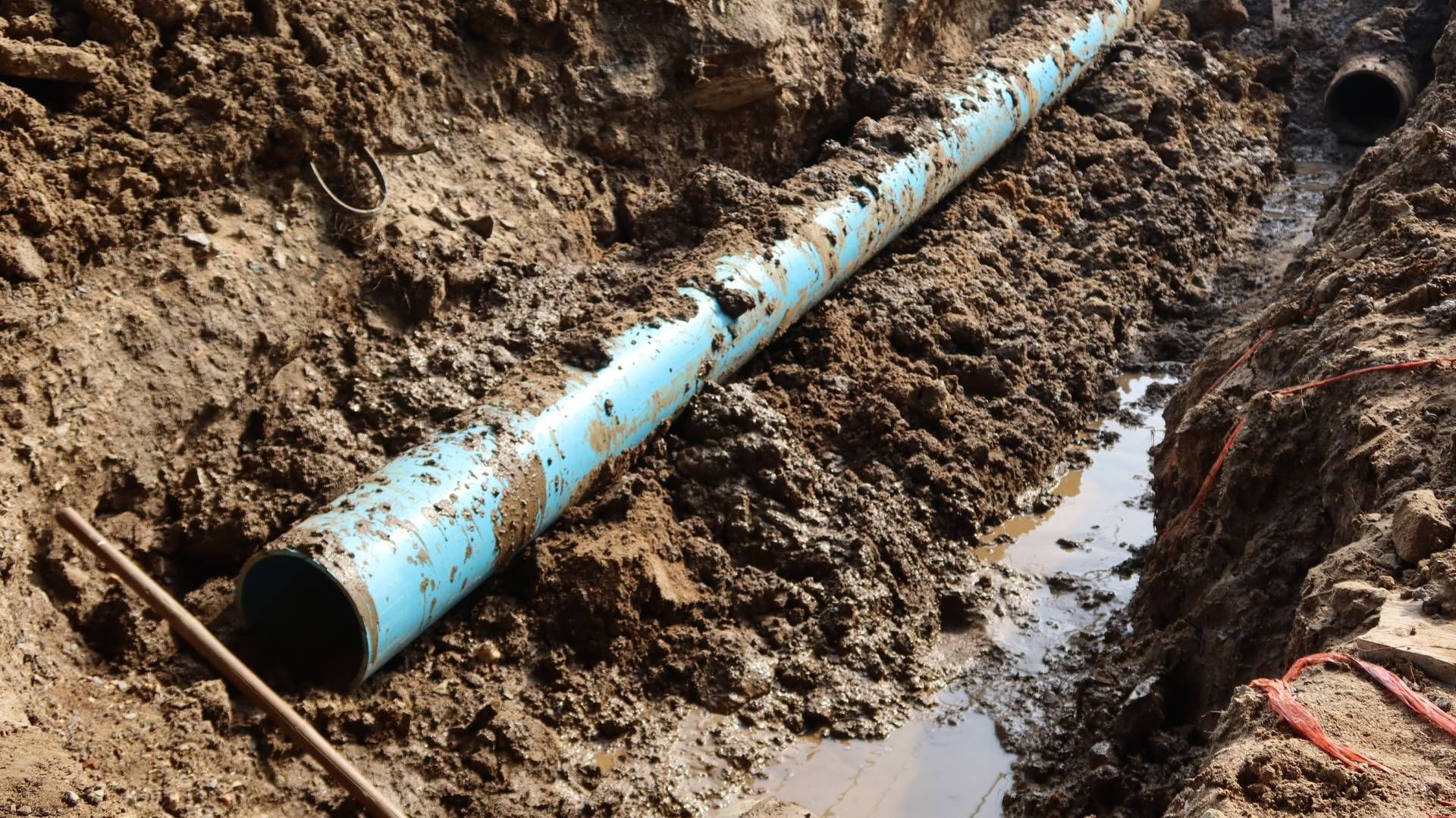 Blue PVC pipe in a muddy trench.
