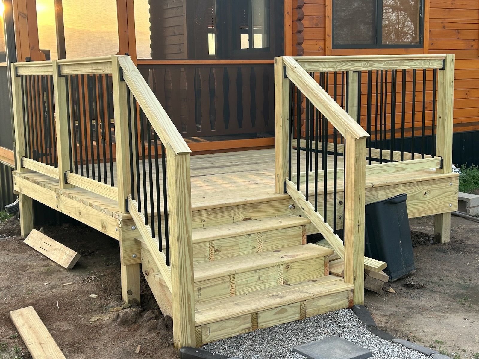 Wooden deck with steps, black railing, and log cabin background.