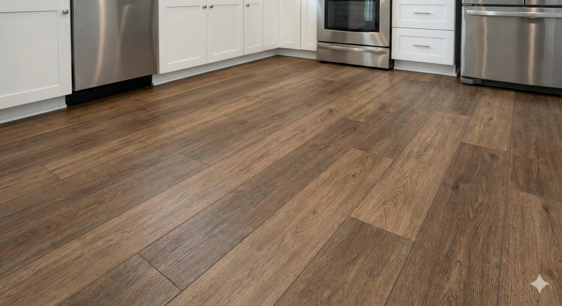 Brown wood-look flooring in a kitchen with white cabinets and stainless steel appliances.