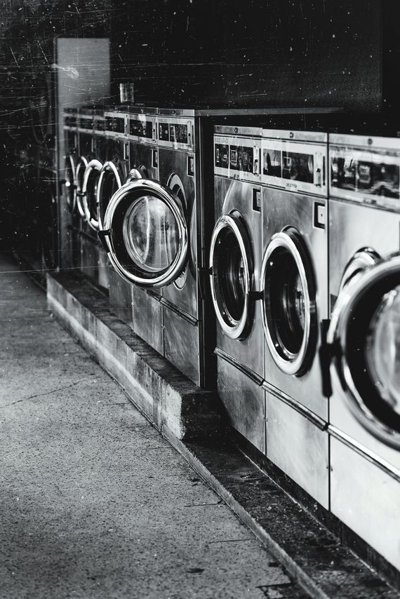 Row of washing machines in a dimly lit laundromat, showing metal exteriors and glass doors.