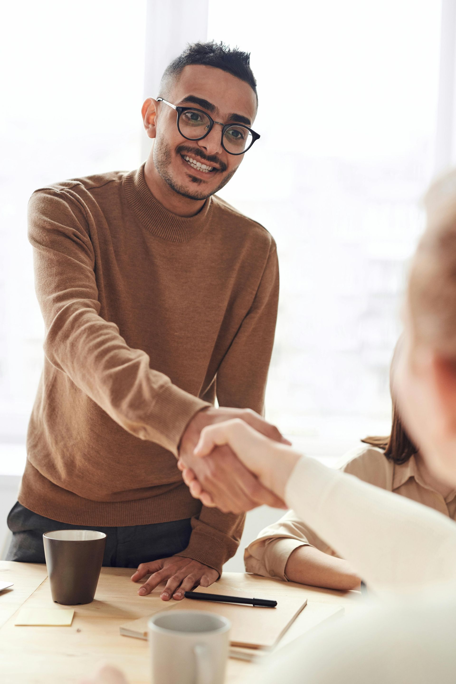 Man in glasses shaking hands with person at table, smiling.