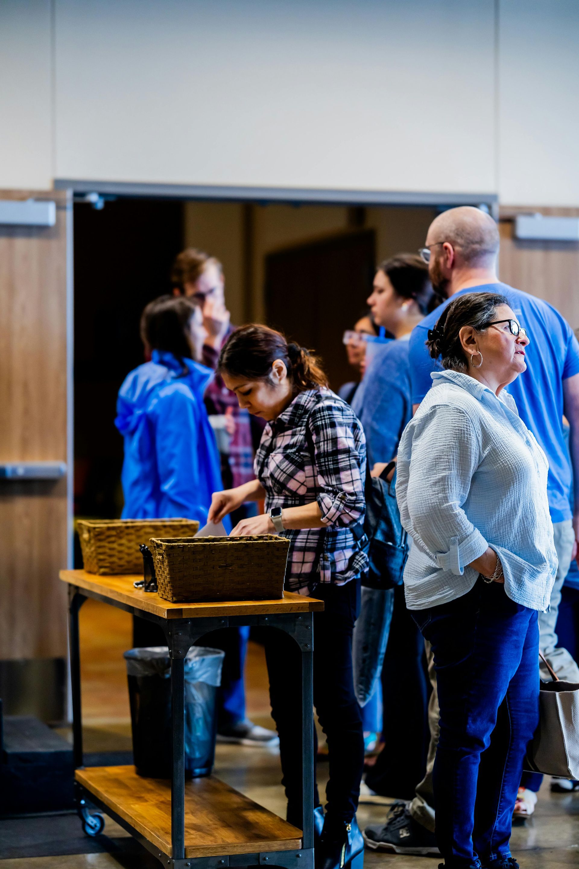 People line up near a doorway, some looking at a table with items on it.