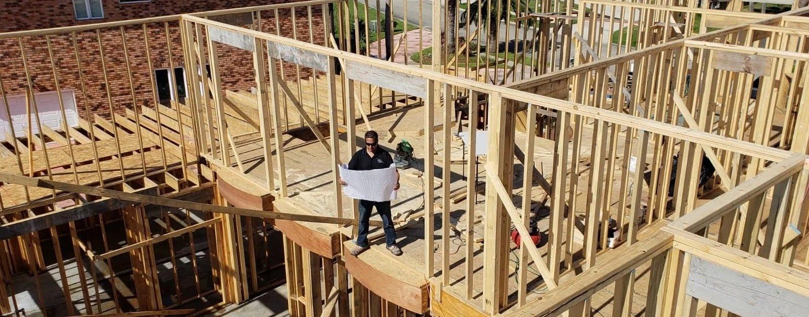 large house in the middle of stick framing while contractor holds plans