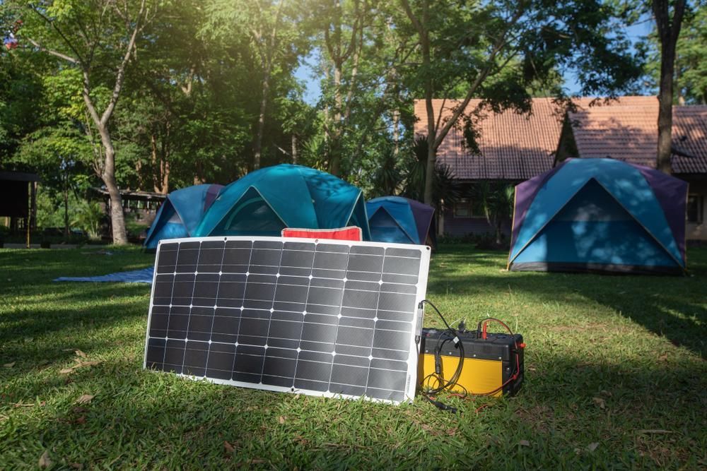 A Solar Panel Is Sitting On Top Of A Lush Green Field Next To Tents — Rainbow Beach Auto Electrics In Rainbow Beach, QLD