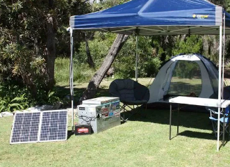 A Tent Is Sitting Under A Blue Canopy Next To A Table And Solar Panels — Rainbow Beach Auto Electrics In Rainbow Beach, QLD