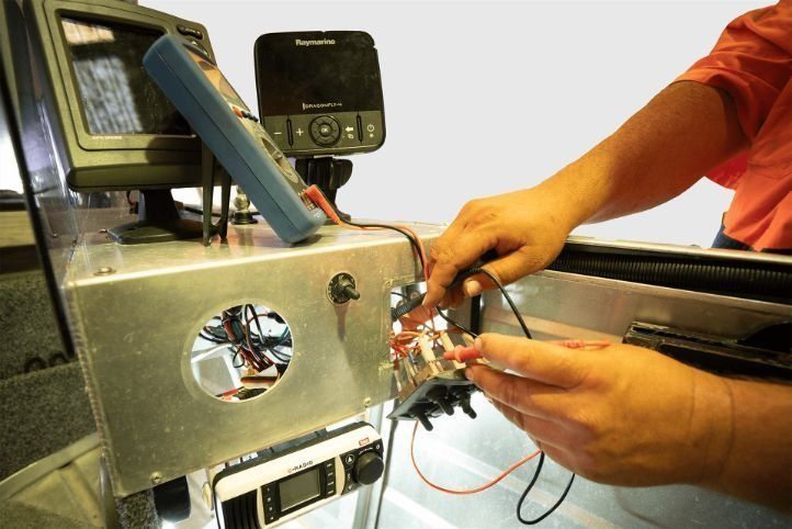 A Man Is Working On A Boat With A Raymarine Device In The Background — Rainbow Beach Auto Electrics In Rainbow Beach, QLD