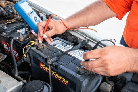 A Man Is Charging A Car Battery With A Charger — Rainbow Beach Auto Electrics In Rainbow Beach, QLD