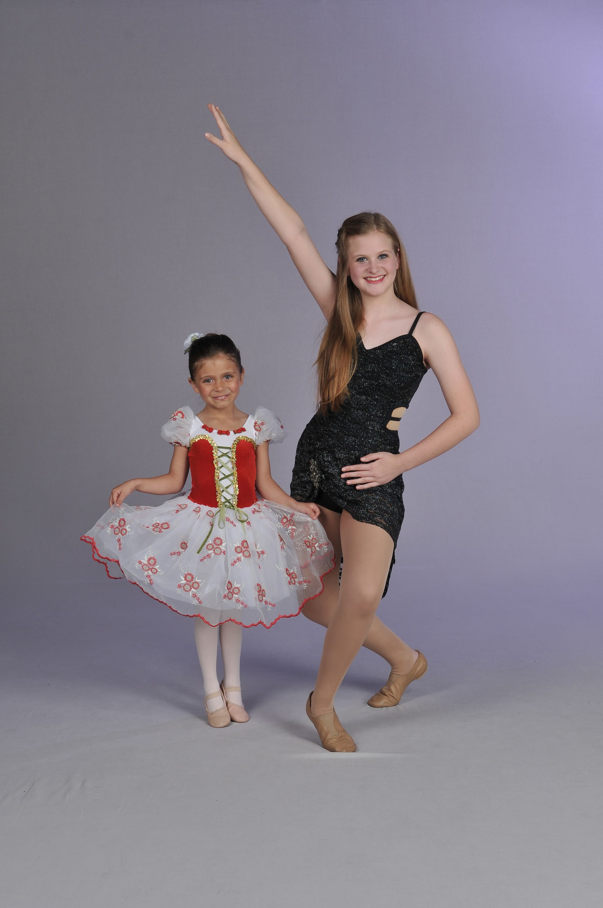 a woman in a black leotard is standing next to a little girl in a red and white dress .