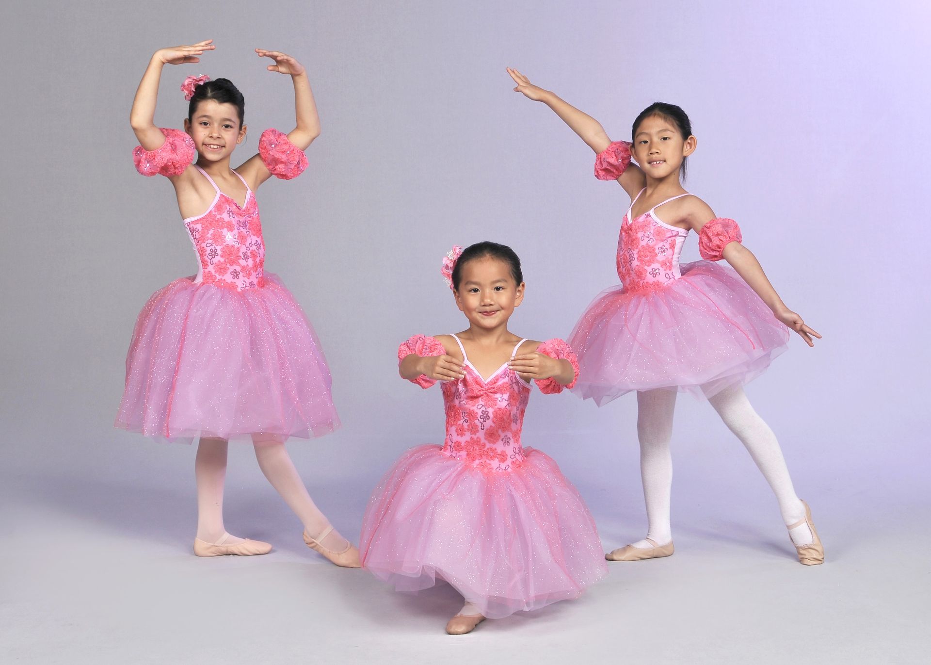 three young girls in pink tutus are posing for a picture .
