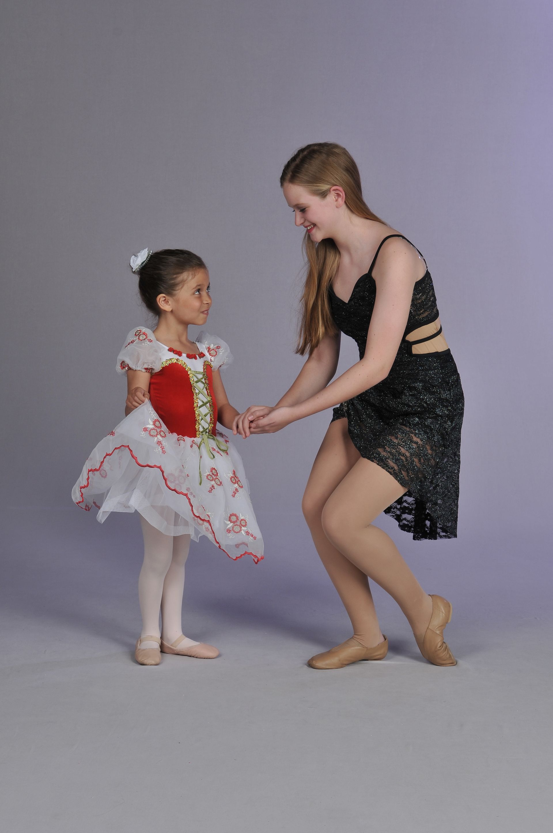 a woman in a black dress is holding the hand of a little girl in a white dress .