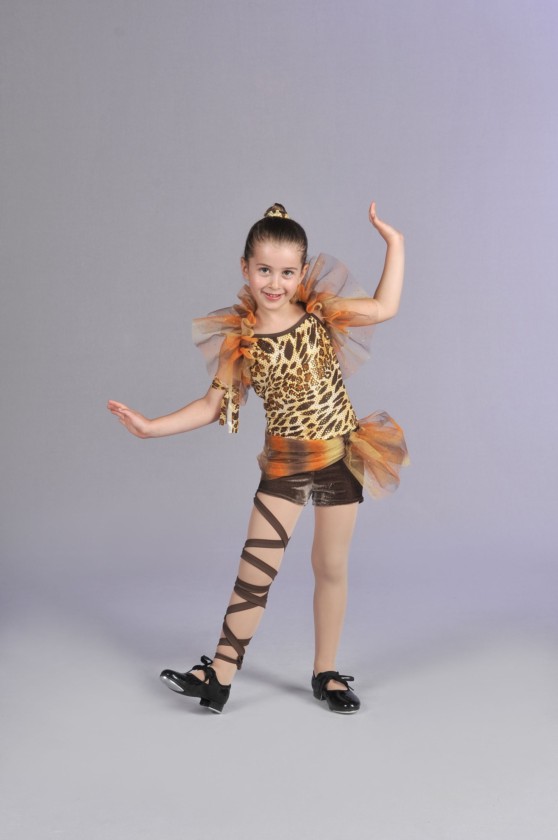 a young girl is weating a golden tutu awith black ballet shoes and is posing for the camera