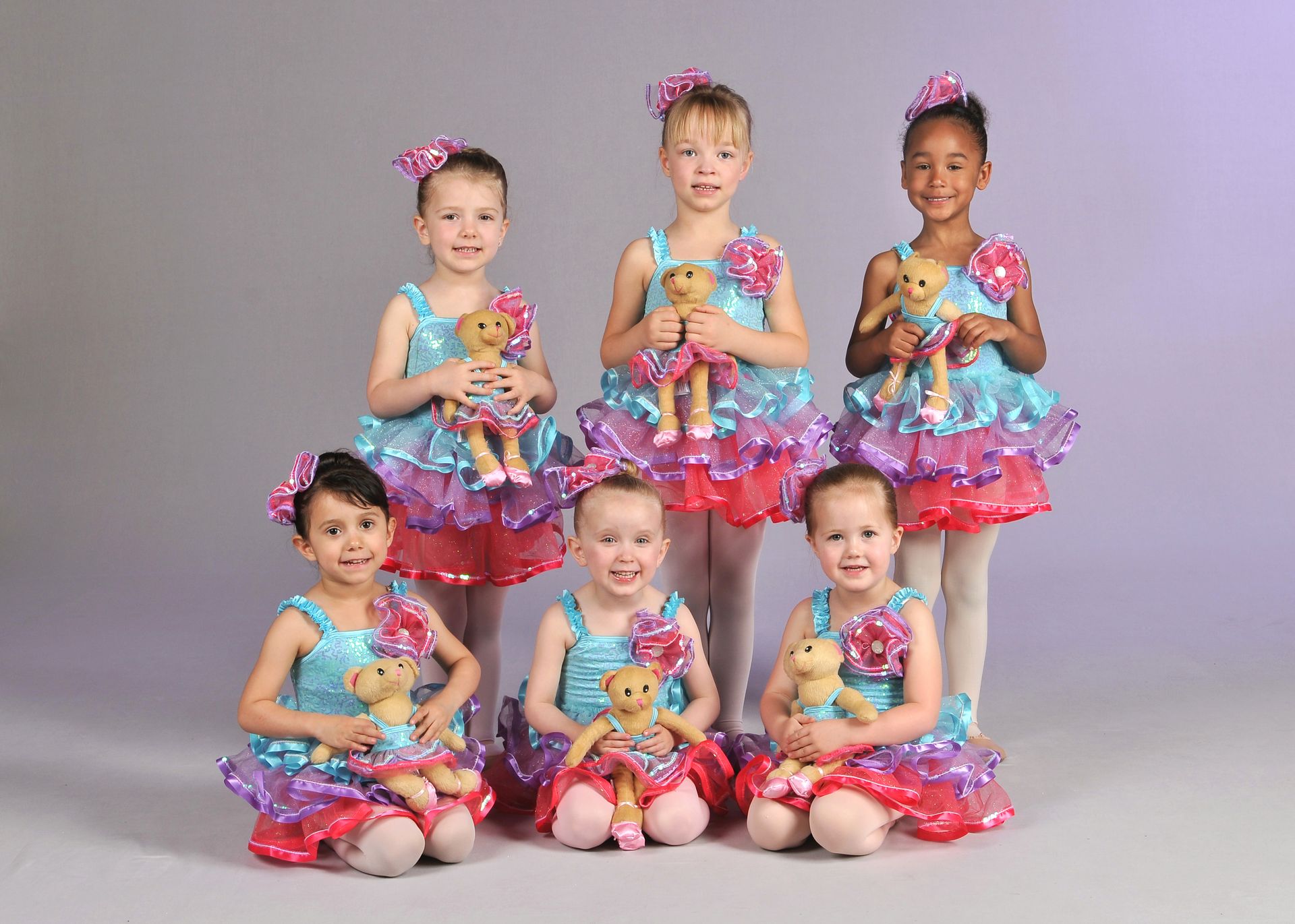 a group of young ballerinas are posing for a picture while holding teddy bears .