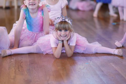 a group of young girls dressed as ballerinas are doing splits on the floor .