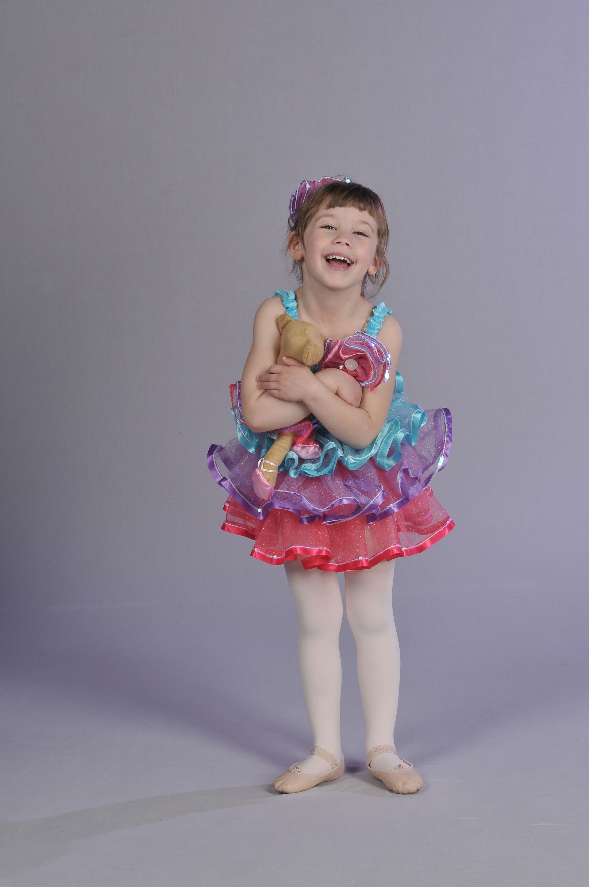a little girl in a colorful tutu is holding a doll .
