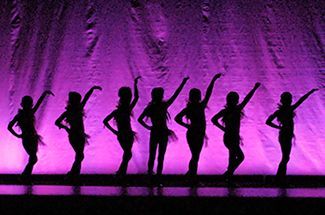 a group of women are dancing in front of a purple curtain