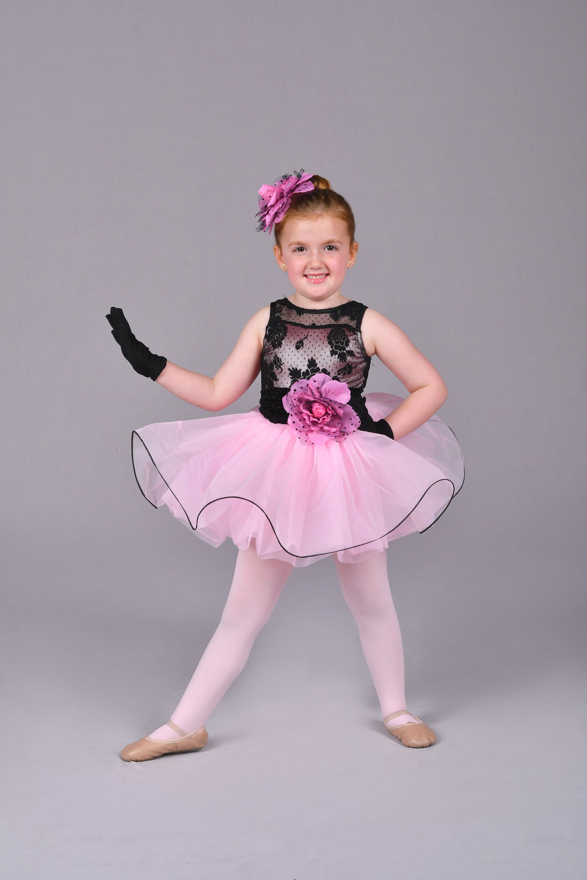 a young girl is wearing her dance recital outfit. it is a pink tutu and a black top with black gloves.