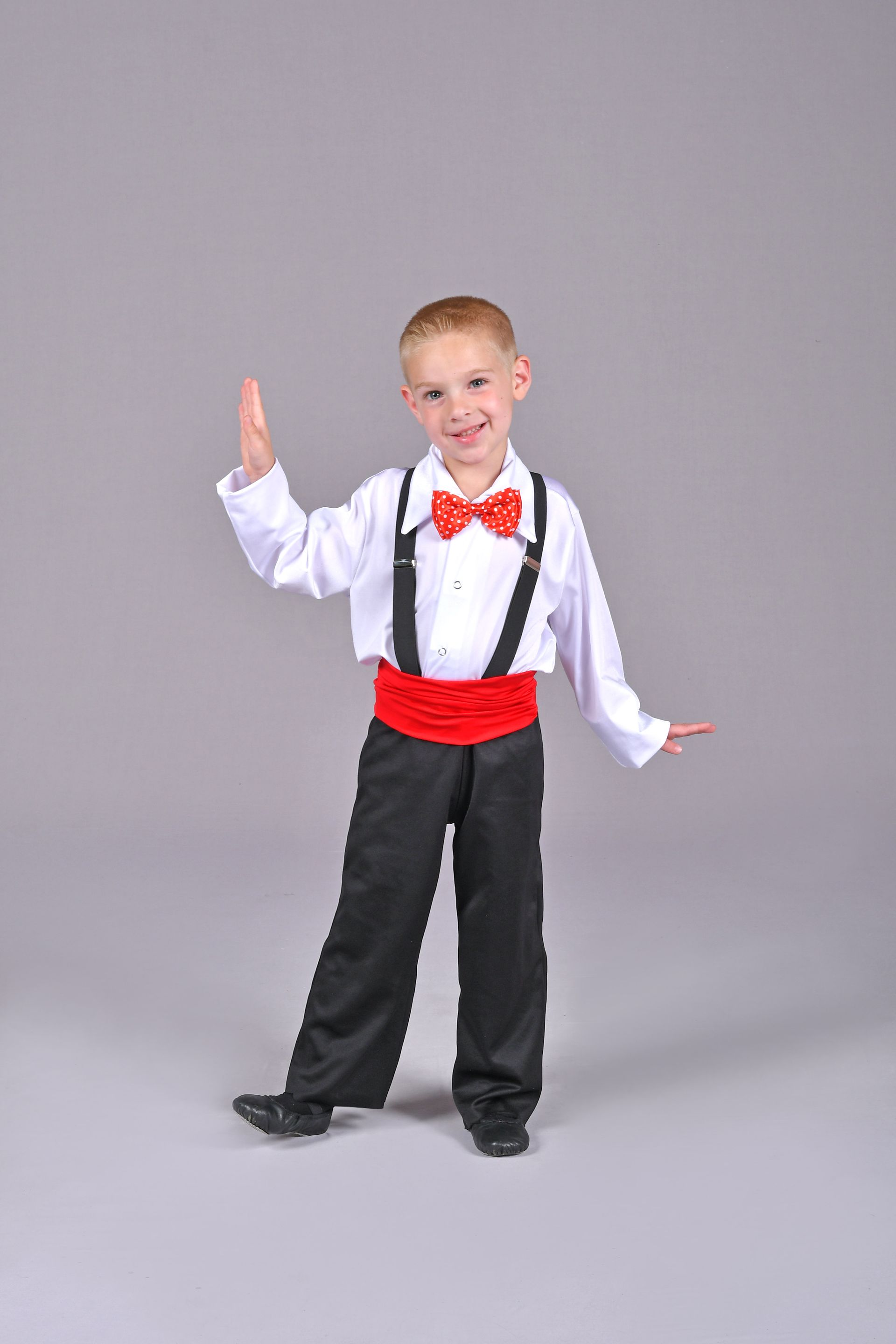 a young boy is wearing a tuxedo with suspenders and a red bow tie .