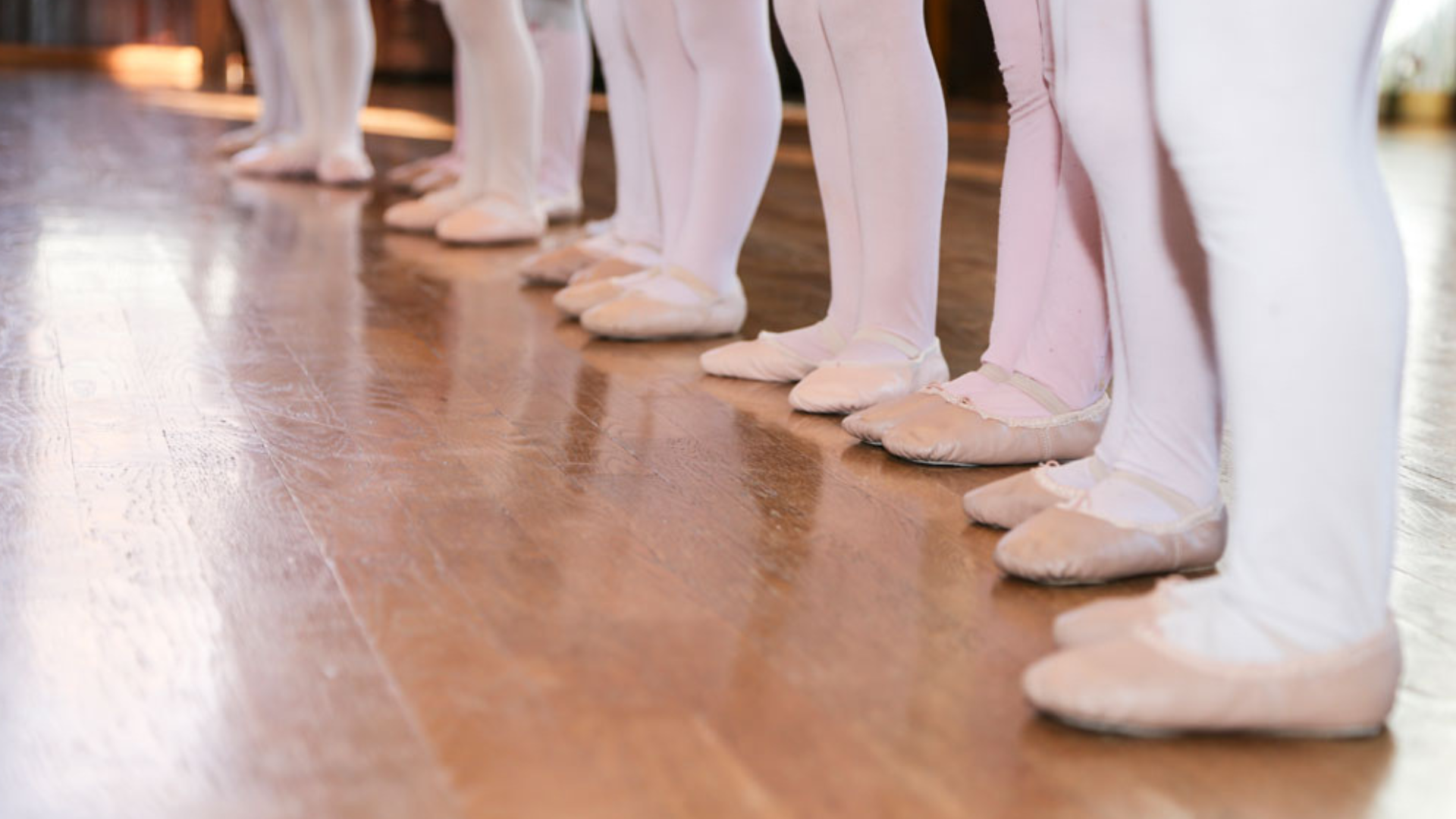 a group of young ballerinas are standing in a row on a wooden floor .
