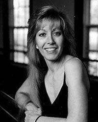 A woman in a black dress is smiling in a black and white photo . Her name is Juanita Wilson and she is the director of the Wilson School of Dance.